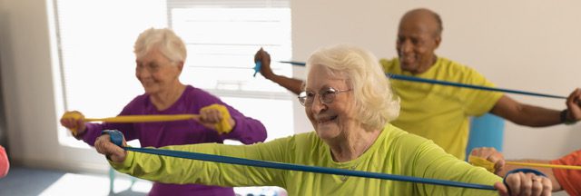 Front view of happy senior people exercising with resistance band in ...
